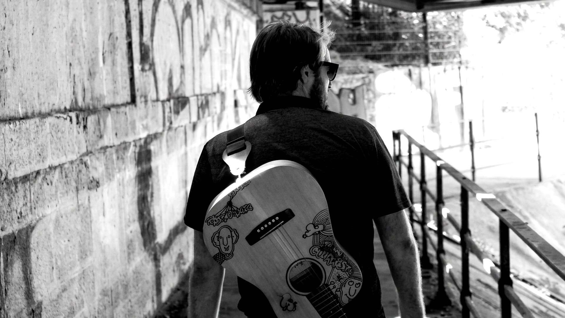 Jean-Michel de dos, guitare sur l'épaule, dans un passage sous un pont